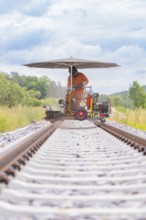 Wide view of a worker in orange on a railway line with an umbrella, grinding work on the Hermann
