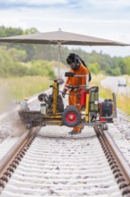 A worker with machines on a railway line, protected by an umbrella, grinding work on the Hermann