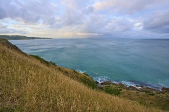 Calm seascape with grassy hill and wide horizon, summer, Nugget Point lighthouse, Ahuriri Flat,