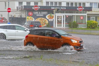 Cars in torrential rain driving through flooded street in town after a heavy downpour, rainfall
