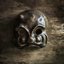 A handcrafted skull mask rests on a weathered wooden surface, highlighting its unique shape and