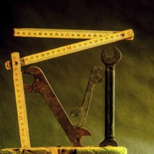 Vintage wrenches and wooden tape measures are arranged creatively against a dark, textured