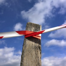 A wooden post stands against a vibrant blue sky, wrapped tightly with red and white barrier tape