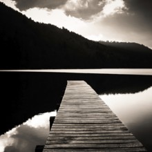A tranquil wooden pier stretches out over the calm waters of Lake Chambon, surrounded by lush hills