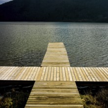 A wooden dock reaches out over serene waters reflecting nearby hills, providing a peaceful spot for