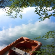 A small boat rests quietly on the tranquil waters of Lake Pavin, surrounded by lush greenery. The