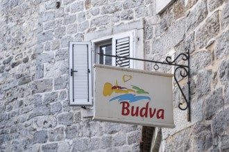 Nose sign with stylised landscape and heart on a stone wall near a window with wooden shop, Budva,