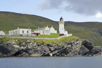 A lighthouse stands on green cliffs with neighbouring buildings, Robert louis Stevenson, boat tour,
