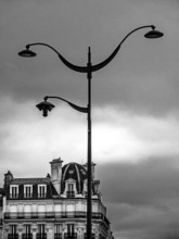 An ornate street lamp rises high against a backdrop of a moody, cloud-filled sky, highlighting the