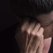 A woman with short hair rests her head on her hand, conveying deep contemplation and introspection