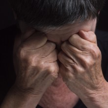 A person sits with their head bowed, hands clasped tightly over their eyes, conveying deep emotion