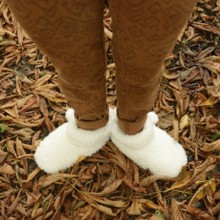 A young woman stands among fallen leaves, wearing warm, fluffy shoes that provide comfort. The