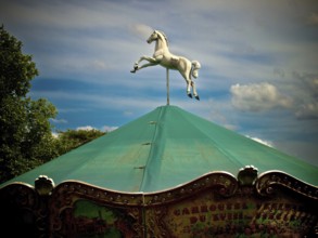 Paris. A carousel topped with a striking white horse in mid-leap stands under a vivid green canopy