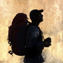 A silhouette of a walker stands against a vibrant, textured backdrop, holding supplies in hand,
