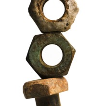 Three worn nuts and a rusty bolt are arranged vertically, highlighting their aged surfaces and