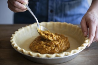 Woman filling homemade pumpkin pie crust with spoon in cozy kitchen scene. Generative AI, AI