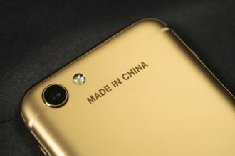 Close-up of engraved Made in China text on the back of a shiny golden smartphone. Concept of