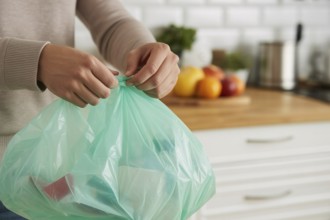 Woman tying up a garbage bag in a home kitchen as part of daily waste disposal. Generative ai, AI