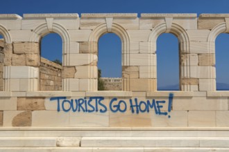 Blue graffiti reading Tourists go home on antique ruin wall with no people present. Generative ai,