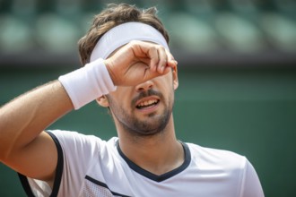 Man in tennis outfit wiping sweat from forehead. Concept for physical effort and athletic