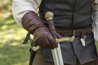 Hand in leather glove holding medieval sword hilt with gemstone. Concept of medieval or LARP