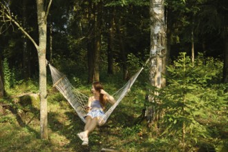 Woman listening to a podcast on a smartphone while relaxing in a hammock in the forest