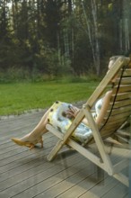 A view through the window at unrecognizable woman relaxing on outdoor terrace in a folding chair