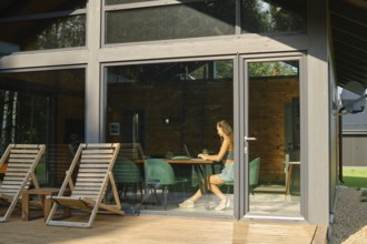 A woman is inside a modern country house with large windows and watches a TV series on a laptop