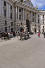 Everyday scene full of tourists and horse-drawn carriages on Michaelerplatz in front of the