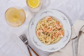 Pasta with shrimp and thyme, served on a white plate, with a glass of white wine, the table is set,