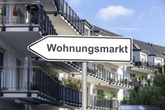 (Photomontage) Sign with the inscription WOHNUNGSMARKT in front of municipal apartment blocks
