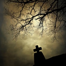 A stone cross emerges from the landscape, silhouetted by the cloudy sky. An isolated tree stretches