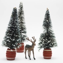 A detailed deer figurine stands in front of two snowy miniature trees, creating a festive