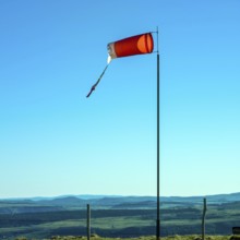 A windsock stands prominently on a pole in Auvergne, gently blowing in the breeze. The clear blue