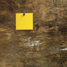 A vibrant yellow sticky note is tacked to a weathered wooden surface, showcasing its artistic charm