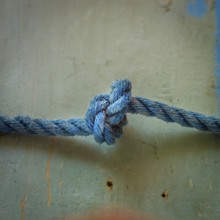 A close-up view reveals an intricately tied blue rope knot resting on a textured surface,