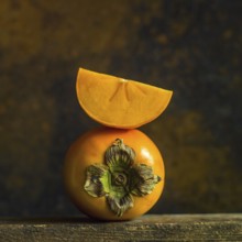 A close-up displays ripe persimmons with a vibrant orange hue, one persimmon features a slice