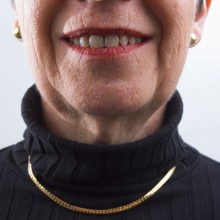 An adult woman is smiling warmly, displaying her confidence and joy. She wears a black turtleneck