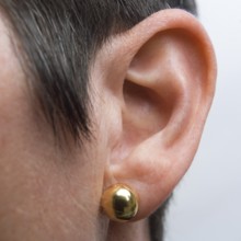 Detailed view of a woman's ear featuring a shiny drop earring. The focus is on the ear structure