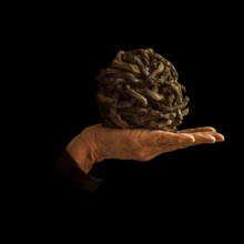 A hand supports a uniquely crafted ball made of intertwined materials, resting against a dark