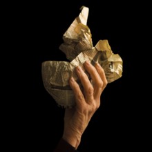 A hand grips a crumpled newspaper, illustrating a mix of emotions and memories. The dark background