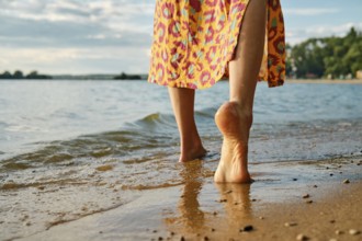 Unrecognizable woman strolls barefoot on a sandy beach, waves gently lapping at her feet. Vibrant