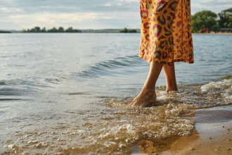 Woman wading in shallow water wearing bright dress by the lakeside during golden hour
