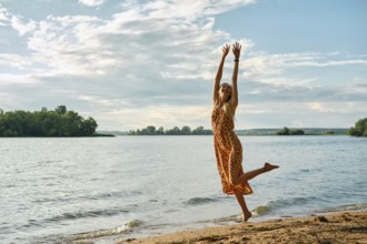 A carefree woman in a colourful sundress dances with joy along the riverbank on a sunny afternoon