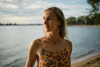 A woman stands near the water's edge, basking in the warm glow of sunset. She wears a colorful