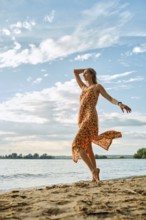 A woman twirls joyfully along the sandy shoreline, wearing a colorful dress. The sun shines