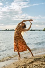 A woman dressed in a vibrant, patterned dress dances gracefully near the edge of a lake. The sun