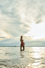 A woman stands in shallow water, enjoying the tranquil surroundings as the sun sets on the horizon.