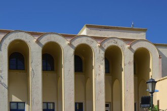 Primary school, Beige-coloured building with large arches against a clear blue sky, Armando