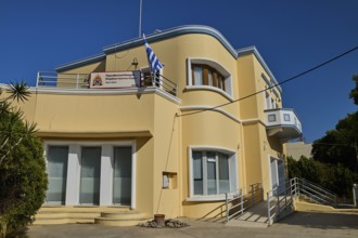 A modern yellow building with balconies and Greek flag, artistically designed, Armando Bernabiti,